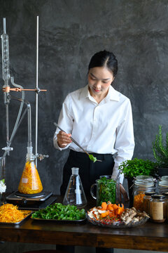 Young Asian Woman Scientist Experimenting with Herbal Extraction Using Laboratory Glassware and Fresh Ingredients