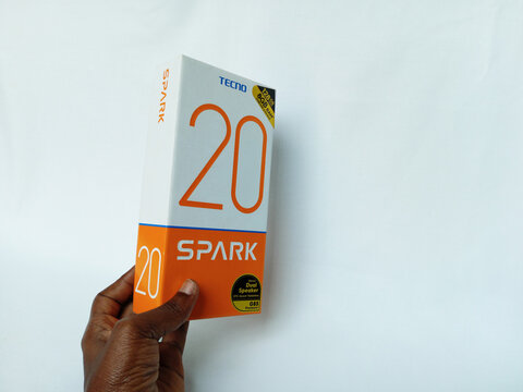 African human hand holding Tecno smartphone paper box package on white background. Spark 20 phone. Android phone with fingerprint, proximity sensor dual flash. Kumasi, Ghana - December 9, 2025