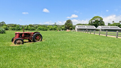 Obraz premium Vintage Red Tractor Parked in a Lush Green Field Under Blue Sky