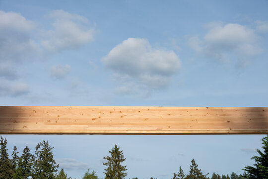 Overhead wood glue laminate, glulam, header beam with blue sky and puffy white clouds in background and fir trees below, housing development project under construction

