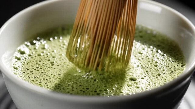 Preparing traditional matcha tea, whisking green powder with bamboo chasen in ceramic bowl, frothy texture, Japanese tea ceremony preparation