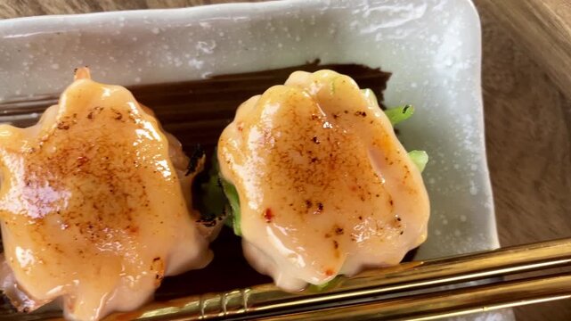 Close up macro view of delicious dim sum shumai topped with creamy torched mentai sauce, served on a rectangular plate with gold chopsticks