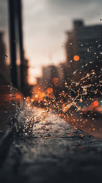 Sparkling water droplets splashing across window ledge against blurred city lights at dusk showing energy motion rainfall urban atmosphere abstract refreshment concept dynamic weather texture