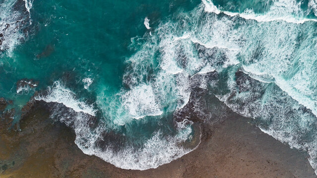 Aerial view of waves crashing against the rocky shoreline of a beach in Indonesia.