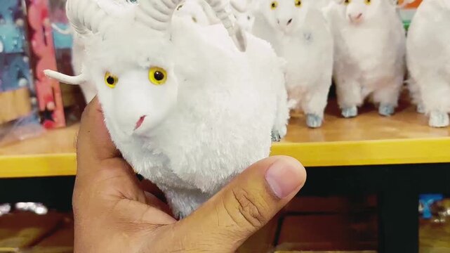 Hand Holding White Plush Ram Toy In A Retail Store