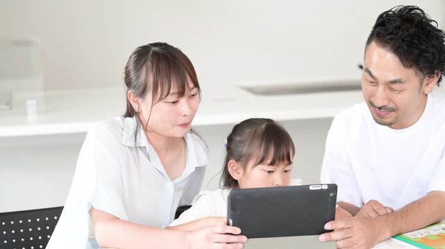 自宅のダイニングやリビングでタブレットを使って家庭学習をする親子3人の家族とデジタル教育のイメージの動画