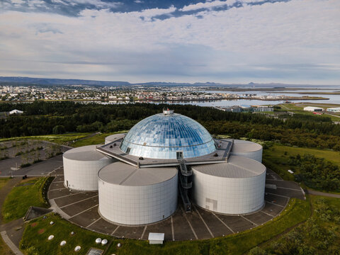 Aerial view of Perlan museum with its iconic glass dome, surrounded by lush greenery, with the bay in the background Reykjavik, Reykjavikurborg, Iceland.