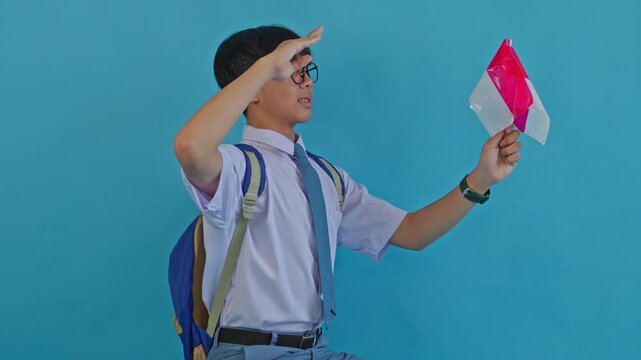 Patriotic Indonesian student in uniform saluting on blue background