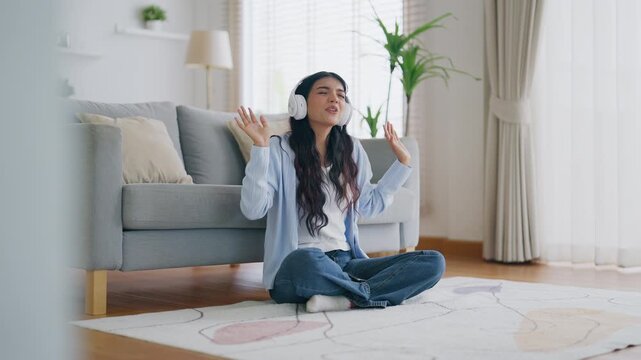 Young asian woman listening to music on couch in living room at home. Happy asia female wearing headset and sitting on the floor