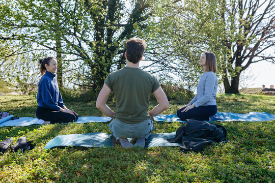 Three Friends Practicing Yoga Meditation Outdoors in a Sunny Park