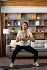 Naklejka premium A fit woman of mixed ethnicity performs a squat exercise on a mat in her living room, focusing on her workout routine
