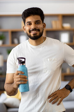 A smiling young Indian man in a white t-shirt holds a blue water bottle, ready for hydration and activity
