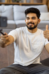 Fototapeta premium A smiling young man of Indian descent gives a thumbs up while recording a video on his smartphone, possibly for social media or a vlog