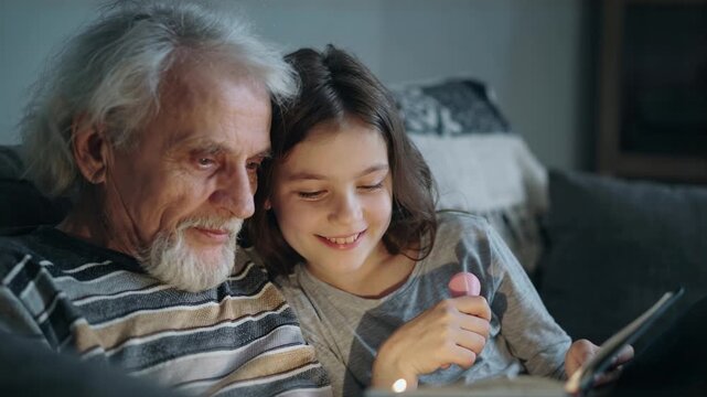 Elderly man and young girl smiling while looking at a tablet