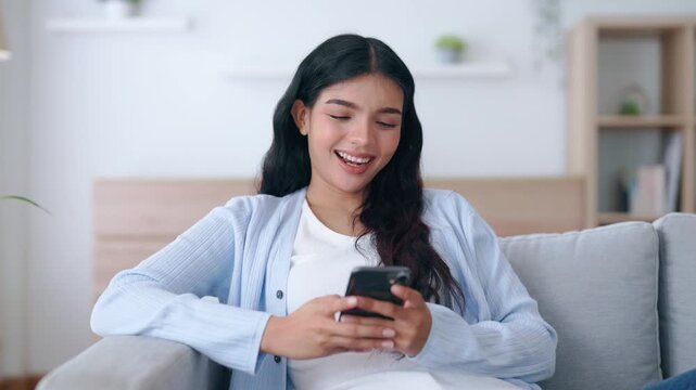 Happy young asian woman relax on comfortable couch at home texting messaging on smartphone, smiling girl use cellphone, chatting online message, shopping online from home