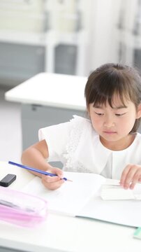 教室で計算ドリルに集中して取り組む幼稚園・小学生位の女の子・塾や学校、受験や勉強、学習のイメージ縦動画　単語帳を見る