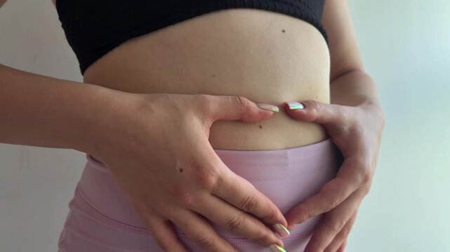 Woman forming heart shape with her hands on her stomach, symbolizing self love, body positivity, digestion health, and the beginning of a healthy pregnancy