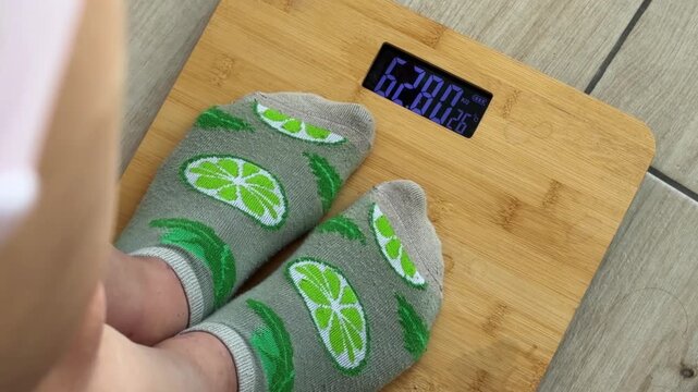 Woman with lime patterned socks stepping on a modern bamboo digital scale for weight control, daily body measurement, diet progress, and healthy lifestyle monitoring
