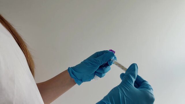 Female laboratory technician wearing blue nitrile gloves preparing blood sample for analysis, unscrewing test tube cap with syringe in hand and isolated on white background