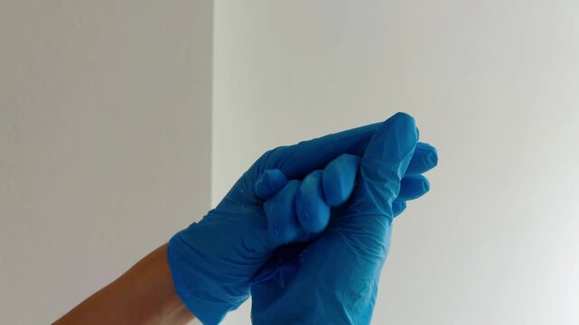 Healthcare worker spraying antiseptic liquid from a bottle on their blue nitrile gloves, sterilizing and rubbing hands for hygiene and safety during a pandemic