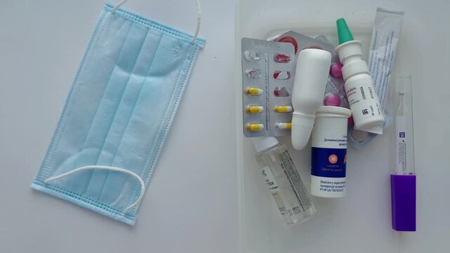 Medical supplies for cold and flu treatment, including pills, nasal spray, and thermometer, with a protective face mask on a white background, concept of healthcare and pandemic