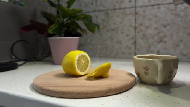 Woman preparing hot lemon water for health, pouring boiling water from a kettle into a cup and adding a fresh lemon slice for a healthy vitamin c morning drink