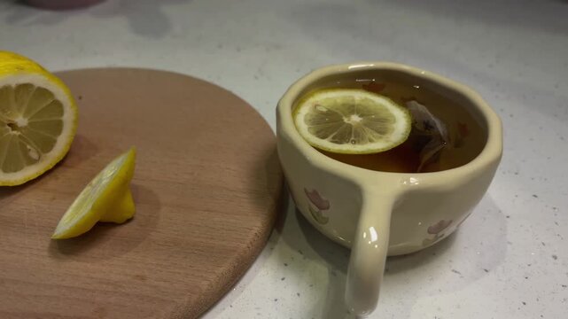 Preparing hot lemon tea by dropping a fresh lemon slice into a warm cup of herbal tea, perfect for a cozy afternoon break or a healthy start to the morning