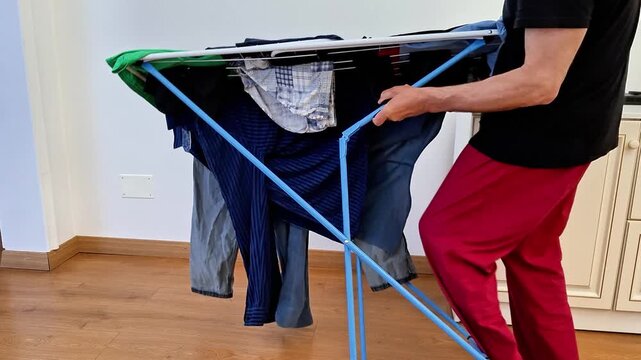 A person folds and carries a collapsible indoor laundry drying rack with fabric cover, demonstrating practical home organization, portable design, efficient storage, and everyday household chores