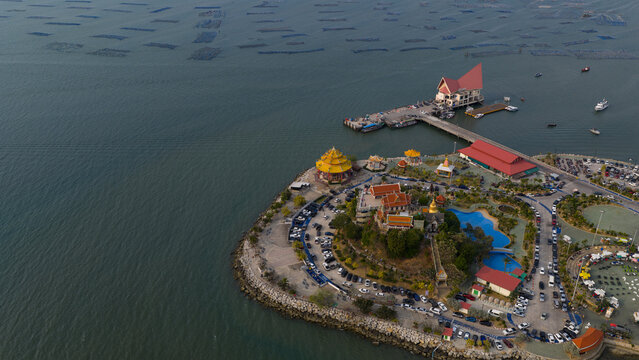 Aerial view of Koh Loi temple complex with its distinctive yellow pagoda, traditional Thai buildings, and a long pier extending into the sea in Si Racha, Chon Buri, Thailand.