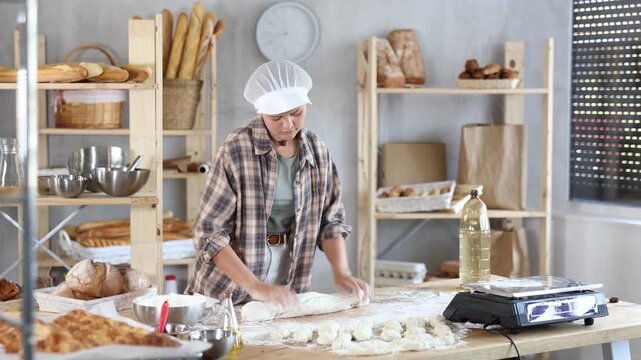 Working in a bakery - girl kneads raw dough to make baguettes or croissants 