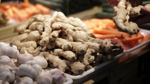  Close-up view of female shop assistant's hands places fresh ginger roots onto display counter in grocery store 