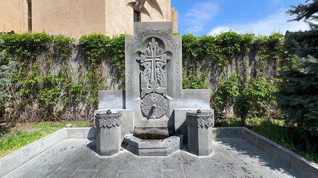 summer urban landscape of Yerevan Armenia the scenic landscape of volcanic tuff stone carved cross monument drinking fountain flowing water historic medieval religious architecture heritage landmark