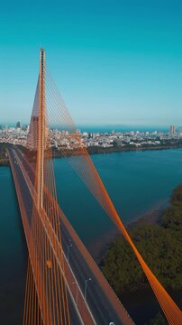 aerial drone view of suspension cable bridge over Han river in Danang, geometric cable-stayed bridge architecture with modern city skyline and roadway, Da Nang Vietnam, 4k vertical video