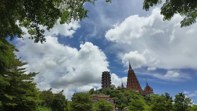 Fast-moving white clouds drift over Wat Tham Sua Tiger Cave Temple framed by dense trees in a daytime timelapse shot.
