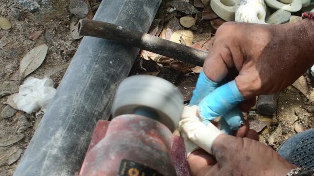 Authentic artisanal work person using a bench grinder or portable polishing motor to clean or grind a small conch held by hand