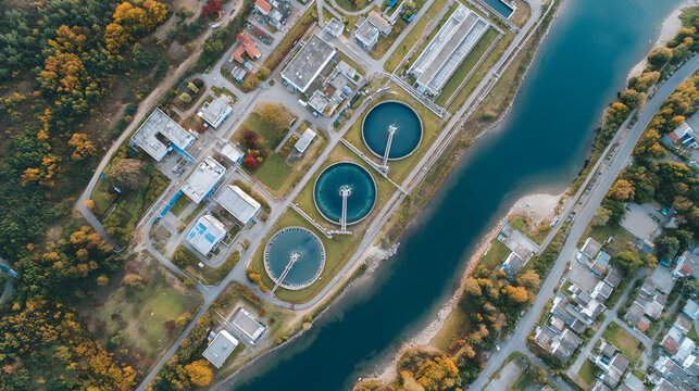 Aerial perspective of a wastewater treatment facility with circular clarifiers and nearby river.