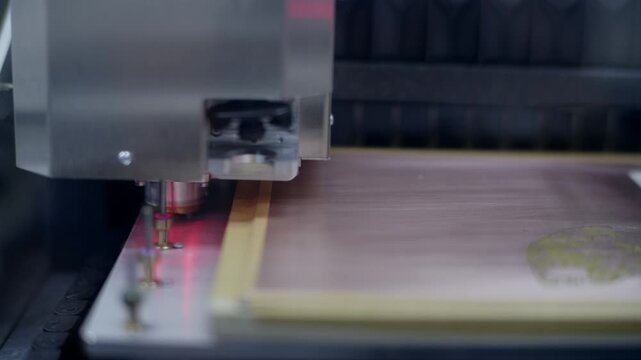 Close up shot of an automated CNC routing machine spindle positioned over a blank copper board to manufacture a printed circuit board, with drill bits in the background.