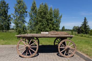 Obraz premium Vintage Wooden Wagon Cart On Pavement With Rustic Spoked Wheels Against Lush Countryside