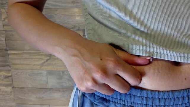 Unhappy woman examining excess belly fat and stretch marks on her abdomen, showing concerns about body image, weight gain, cellulite, and postpartum body changes