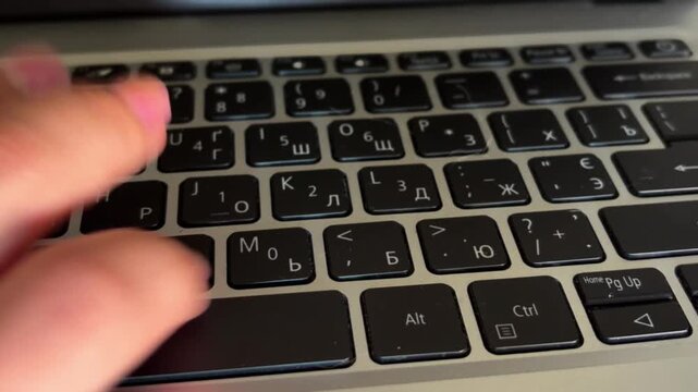 Woman with pink manicure typing on a laptop keyboard, female fingers pressing black keys with latin and cyrillic letters, close up view of business communication
