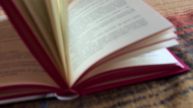Open book pages turning in the wind, a compelling story of knowledge, education, and learning. Close up on a hardcover red book lying on a textured surface