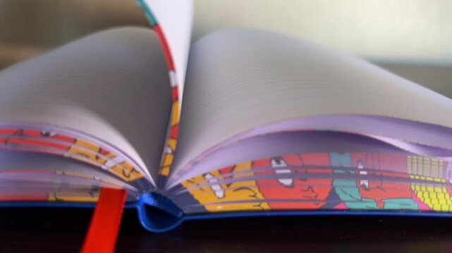 Close up of notebook pages quickly turning, revealing colorful cartoon designs on the edges and a vibrant red bookmark, symbolizing reading, learning, and creativity