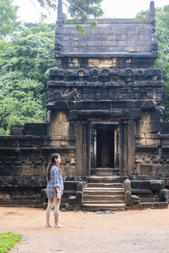 A woman tourist looking at the ancient Nalanda Gedige stone temple in Sri Lanka, a unique historic site featuring a blend of Hindu and Buddhist architecture surrounded by trees.