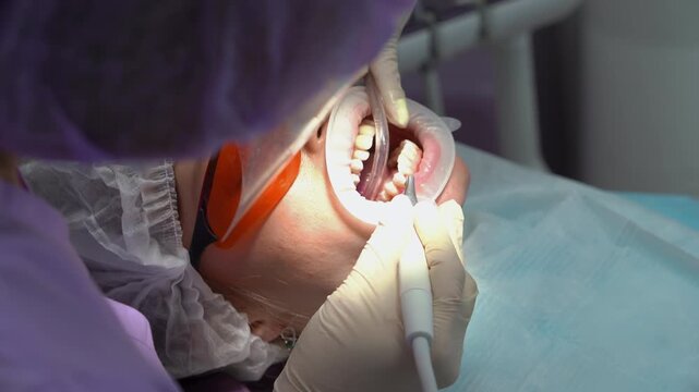 Closeup woman in dental glasses at the clinic. Dentist sucks the patient's saliva with a saliva pump, uses professional dental instruments