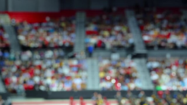Blurred crowd of spectators sitting in stadium stands during large public event, abstract audience background