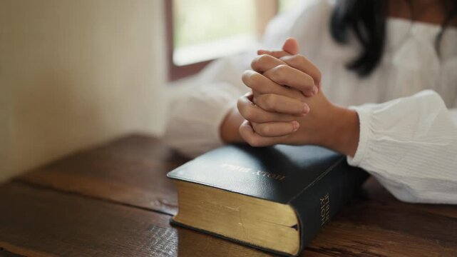 child hand clasped in prayer over the Holy Bible on a wooden table to pray and praise worship. praying to god. Christianity, spirituality, belief, religion, and faith with copy space.