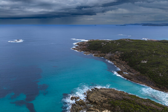 Aerial view of Conspicuous Cliff with turquoise waters crashing against the rocky coastline under dark storm clouds in Nornalup, Western Australia, Australia.