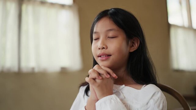 Child pray concept. Happy Asian girl with folded hands to prayer and praise worship in church. kid praying to god. Christianity, spirituality, religion and faith.