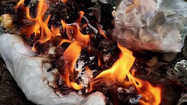 High angle close up shot of intense bright flames burning and shrinking plastic household trash.