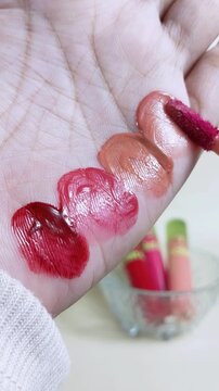 Applying bright red lip stain to palm skin using a makeup brush applicator. Vertical close up shot. Beauty product presentation, bold pigment texture.